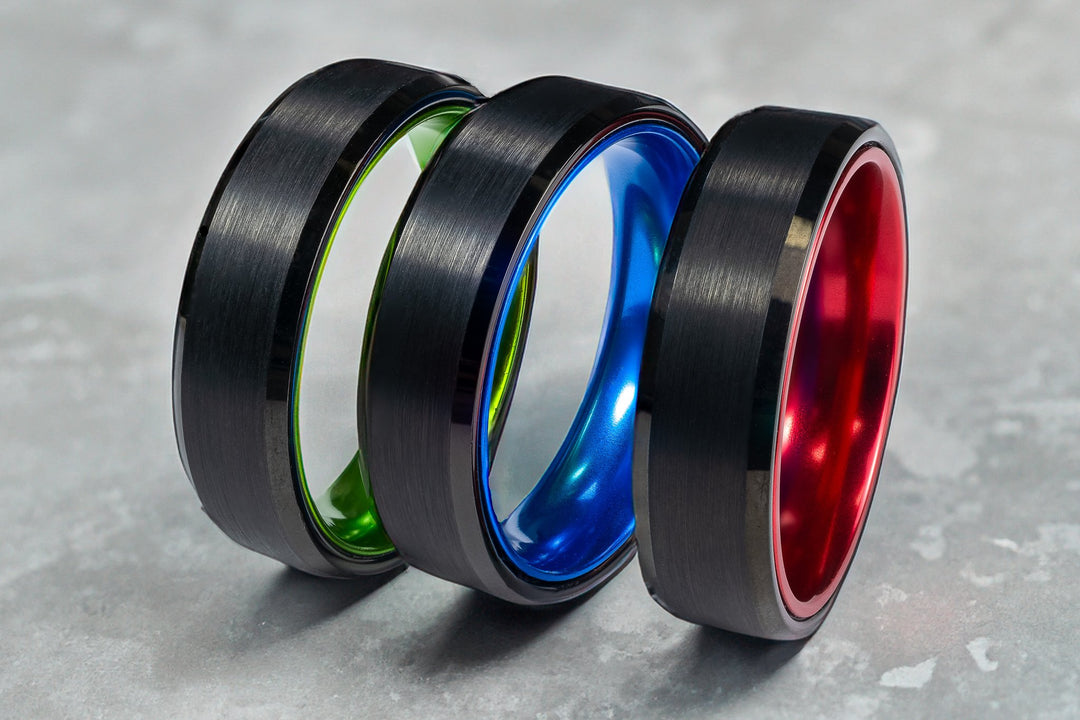 3 Tungsten carbide wedding bands standing up right with a red, blue and green interior and a black brushed exterior in 6mm.