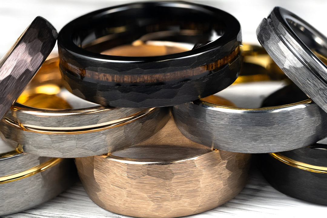 A stack of tungsten carbide wedding bands on top of each other in varying sizes, colors and finishes.