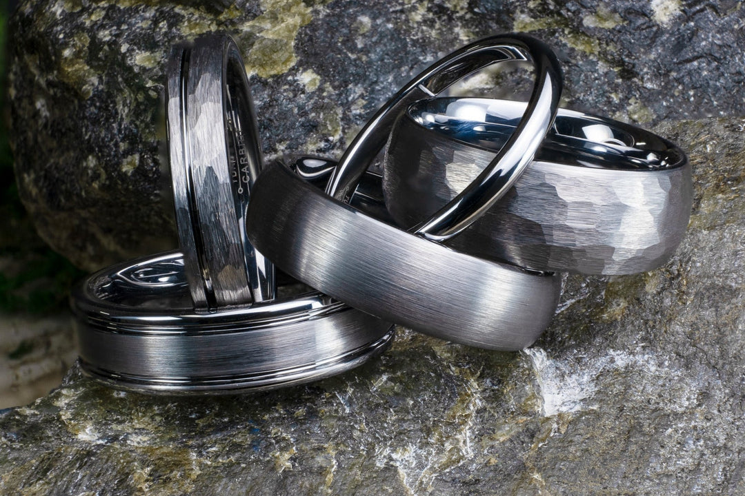 Silver tungsten carbide rings in many mm width sizes and finshes on top of a stone backdrop.