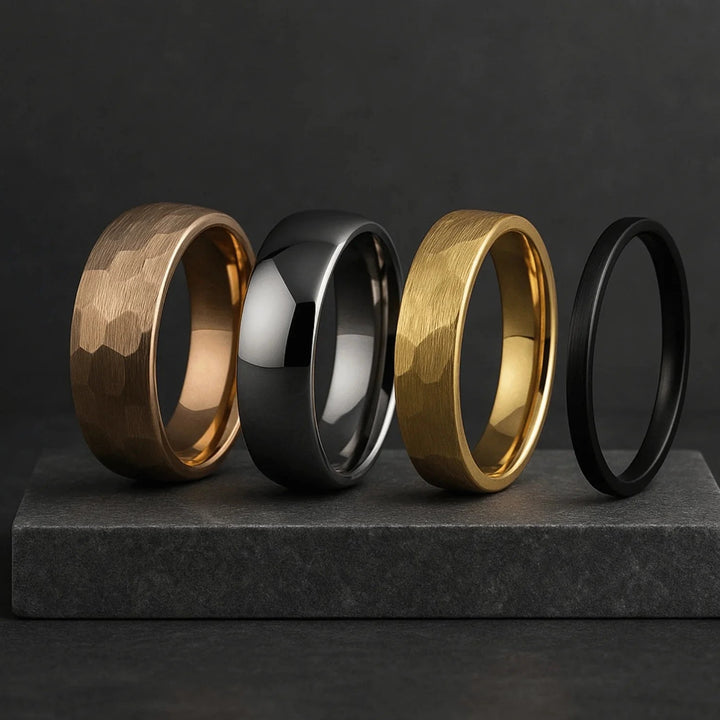 Four rings in gold, silver, and black on a dark gray platform with a black background