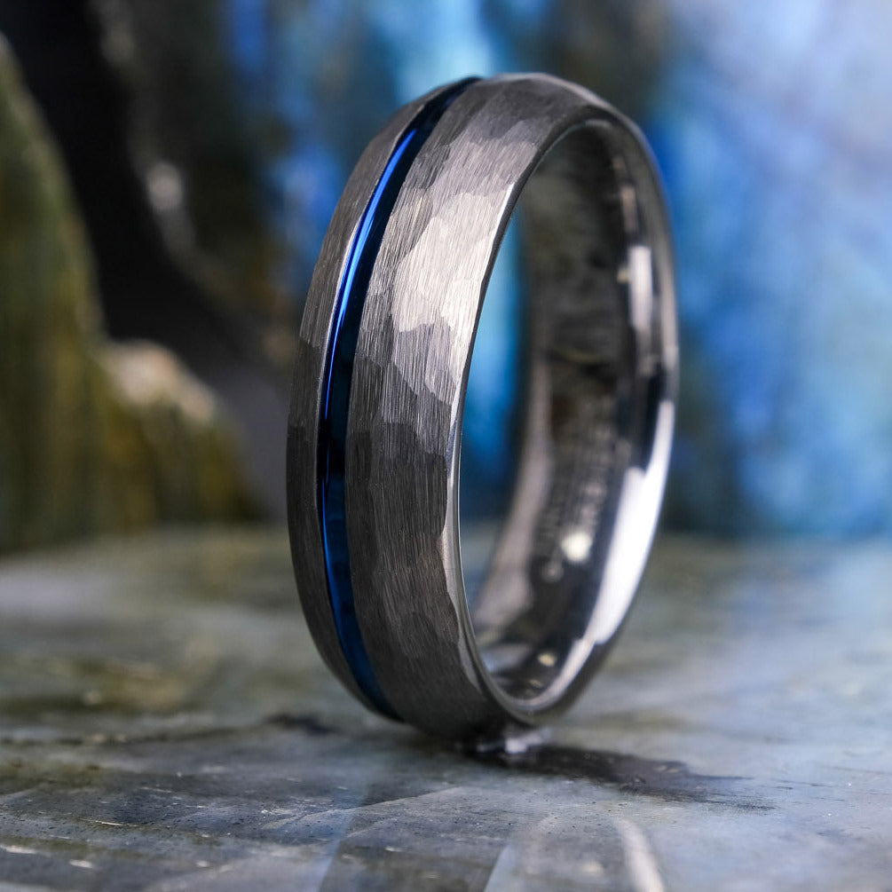 Silver ring with a blue stripe on a stone surface with a blurred natural background