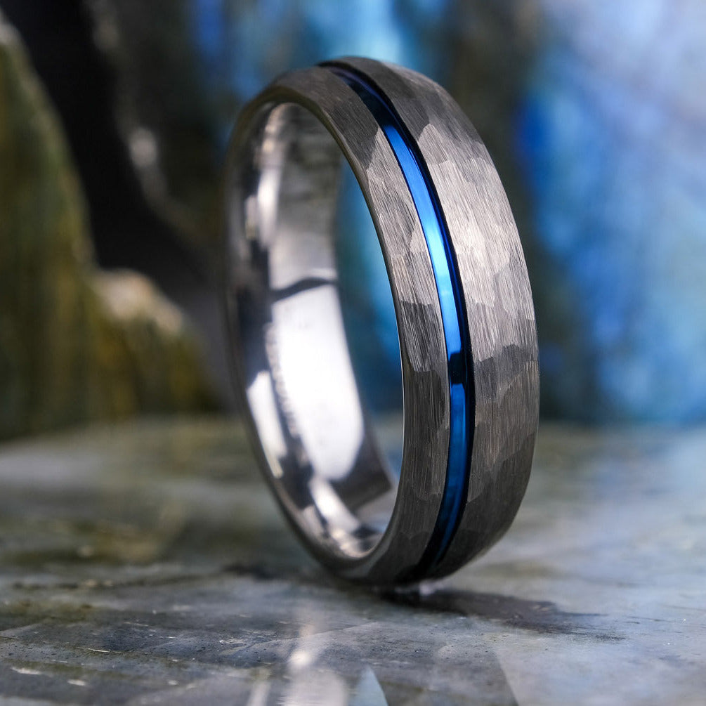 Silver ring with a blue stripe on a stone surface with a blurred natural background