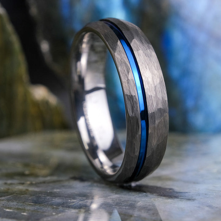 Silver ring with a blue stripe on a stone surface with a blurred natural background