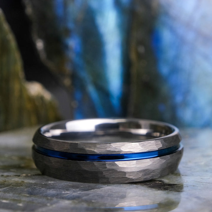 Silver ring with a blue stripe on a stone surface with a blurred natural background