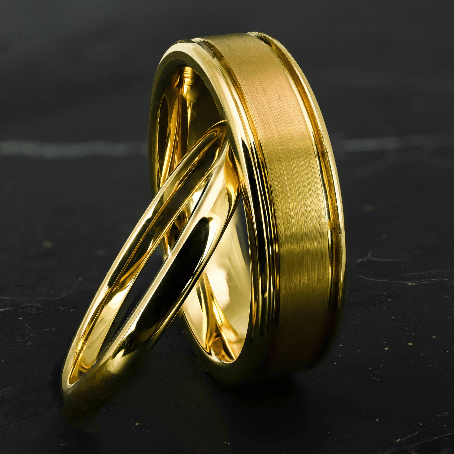 His and hers polished yellow gold wedding bands on a black stone surface.