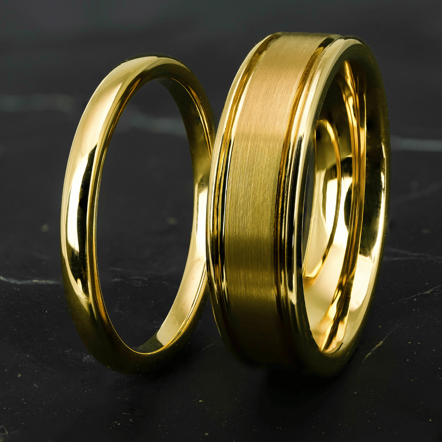 His and hers polished yellow gold wedding bands on a black stone surface.