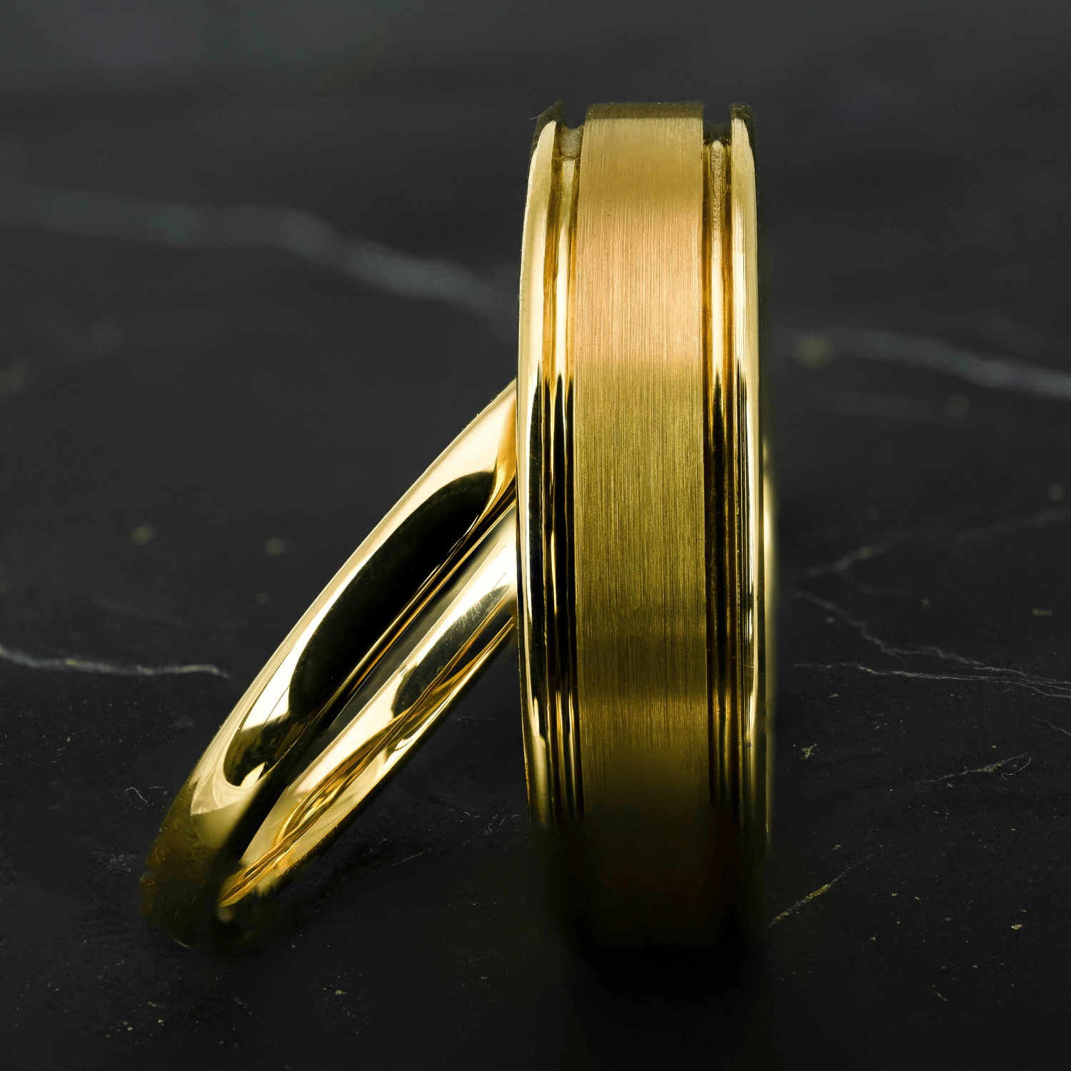His and hers polished yellow gold wedding bands on a black stone surface.