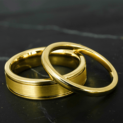His and hers polished yellow gold wedding bands on a black stone surface.