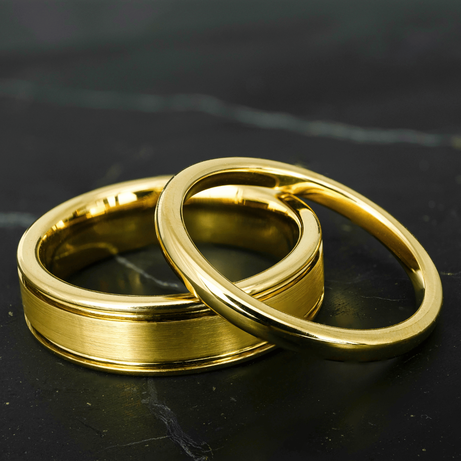 His and hers polished yellow gold wedding bands on a black stone surface.