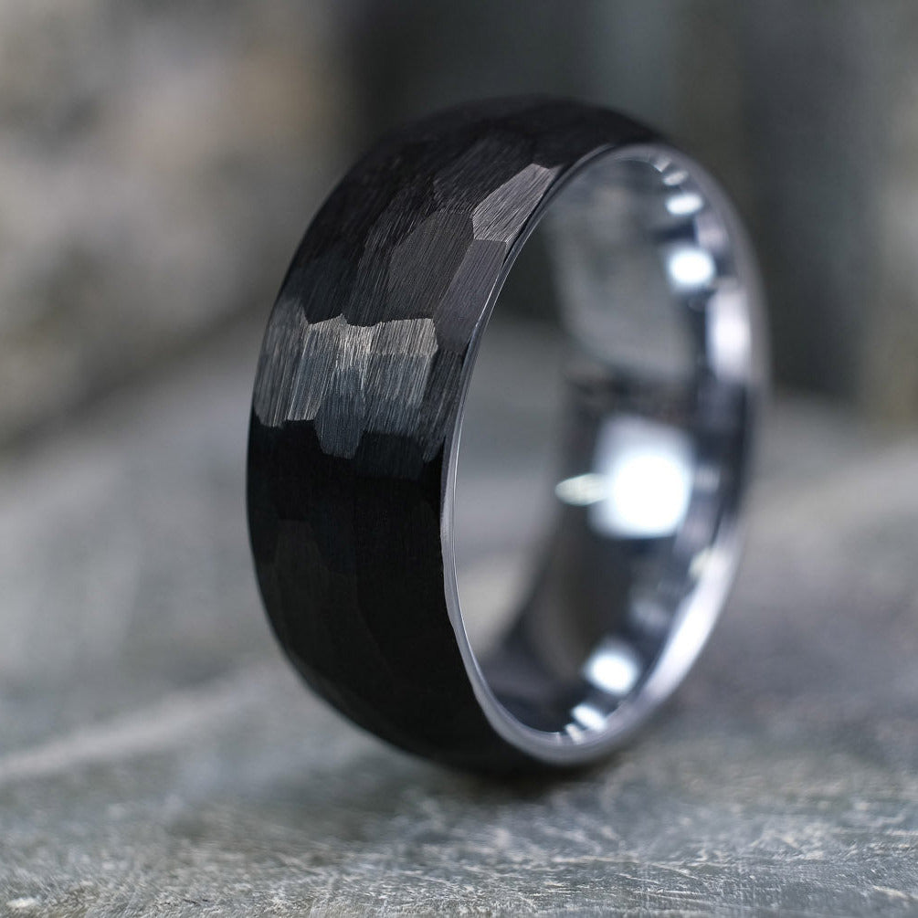 Black Brushed tungsten carbide wedding band with a silver polished interior standing up on a textured grey stone.