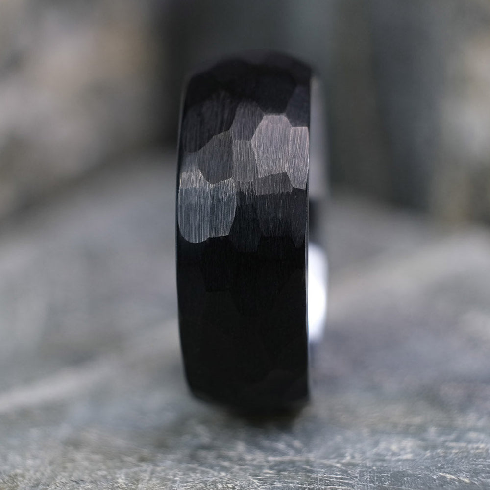 Black Brushed tungsten carbide wedding band with a silver polished interior standing up on a textured grey stone.