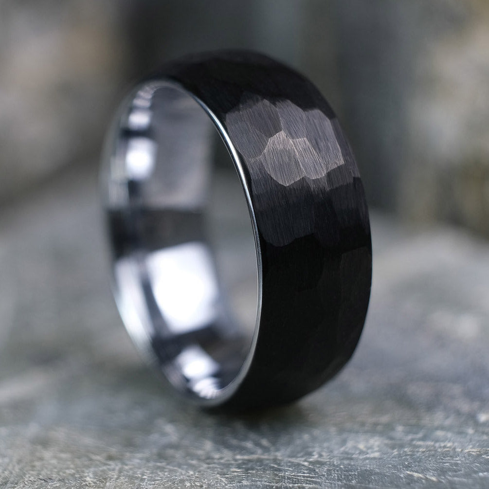 Black Brushed tungsten carbide wedding band with a silver polished interior standing up on a textured grey stone.