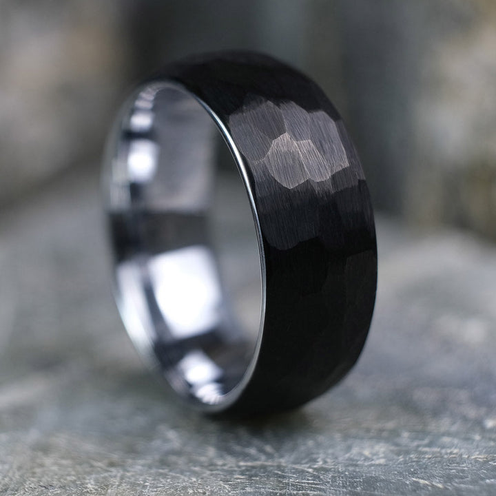 Black Brushed tungsten carbide wedding band with a silver polished interior standing up on a textured grey stone.