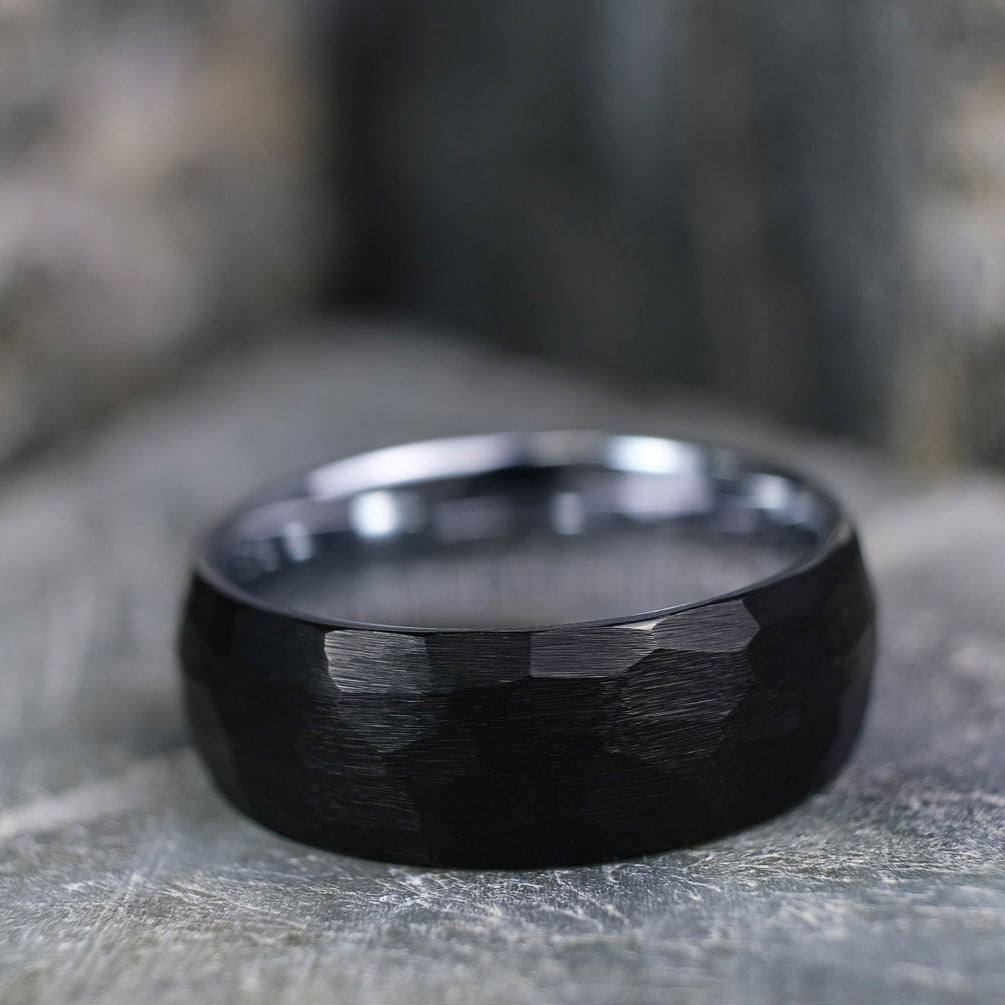 Black Brushed tungsten carbide wedding band with a silver polished interior standing up on a textured grey stone.