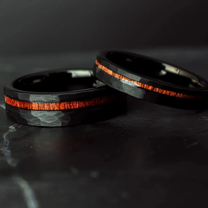 Black hammered koa wood stripe his and hers 6mm ad 4mm band on a black stone.