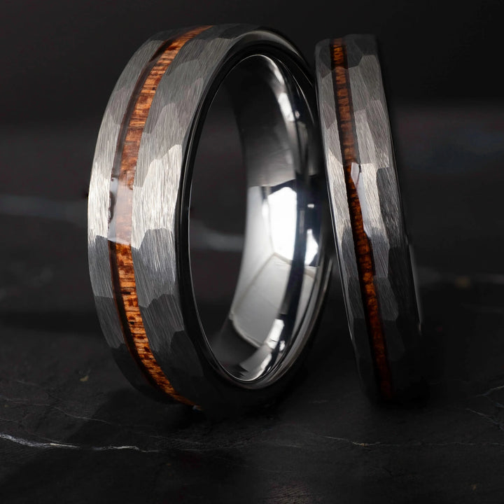 Koa wood his and hers silver hammered tungsten carbide wedding bands in 6mm and 4mm on a dark marble slab.