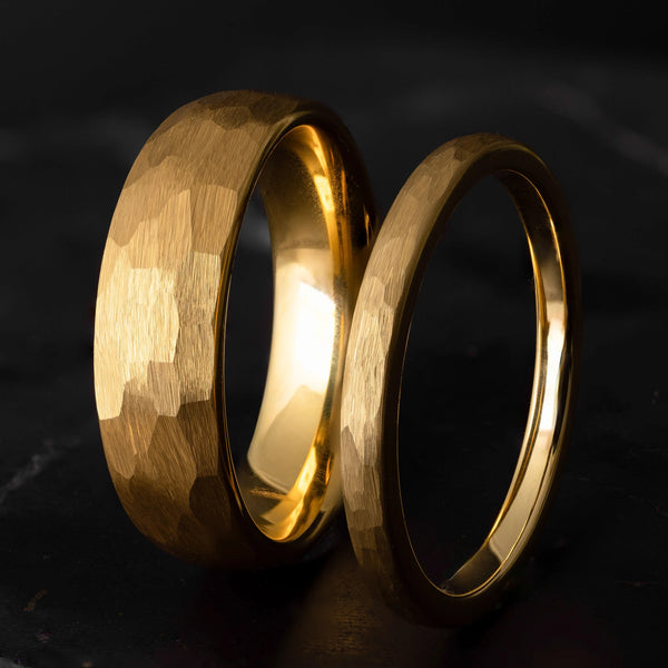 His and hers yellow gold hammered tungsten carbide wedding bands in 6mm and 2mm on a black marble stone. 