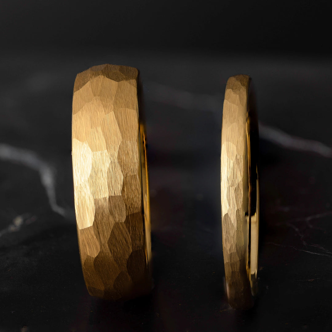 His and hers yellow gold hammered tungsten carbide wedding bands in 6mm and 2mm on a black marble stone. 