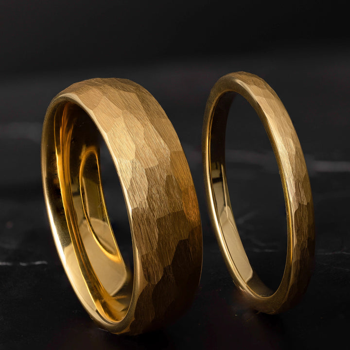 His and hers yellow gold hammered tungsten carbide wedding bands in 6mm and 2mm on a black marble stone. 
