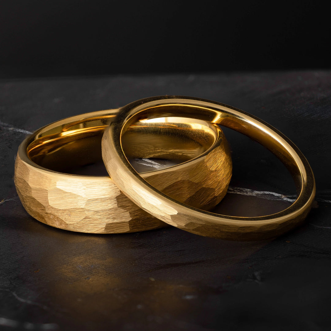 His and hers yellow gold hammered tungsten carbide wedding bands in 6mm and 2mm on a black marble stone. 