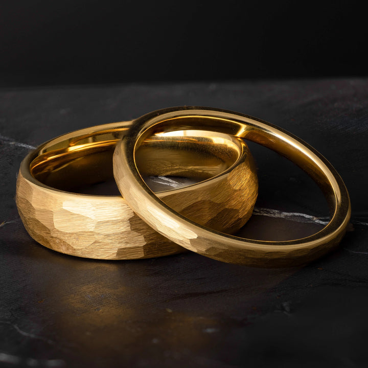 His and hers yellow gold hammered tungsten carbide wedding bands in 6mm and 2mm on a black marble stone. 