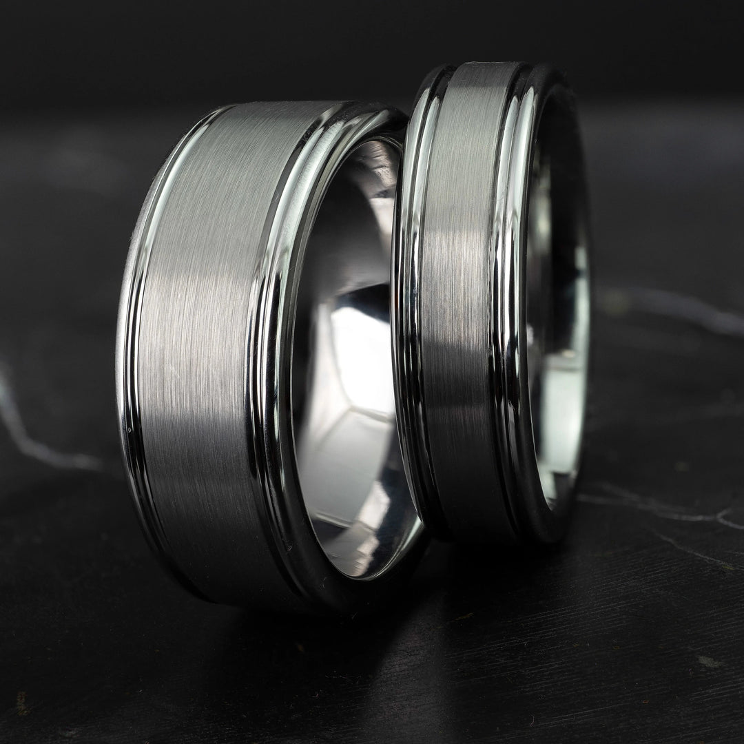His and hers silver polished edge set 6mm and 8mm tungsten carbide bands on a black marble stone.