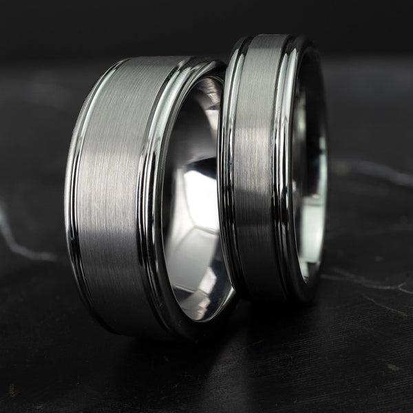 His and hers silver polished edge set 6mm and 8mm tungsten carbide bands on a black marble stone.