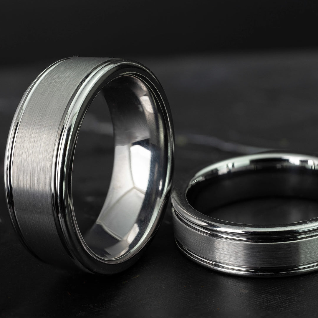 His and hers silver polished edge set 6mm and 8mm tungsten carbide bands on a black marble stone.