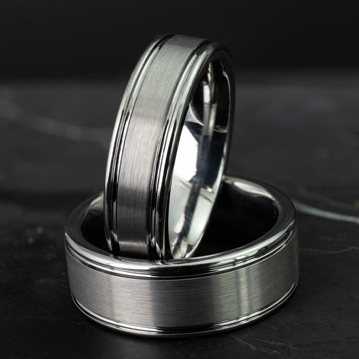 His and hers silver polished edge set 6mm and 8mm tungsten carbide bands on a black marble stone.
