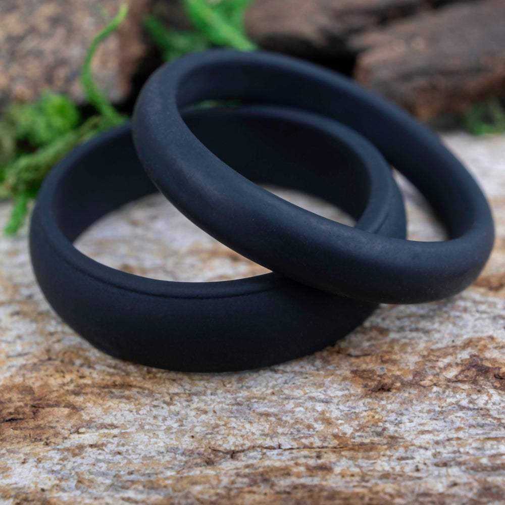 Two black silicone bands on a textured surface with greenery in the background