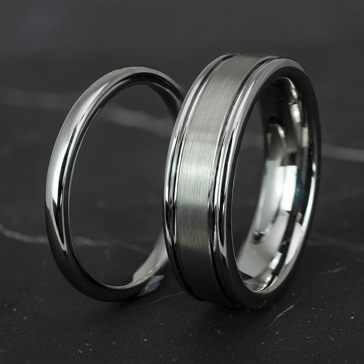 His and hers silver polished 2mm and 6mm tungsten carbide wedding bands on top of black marble stone.