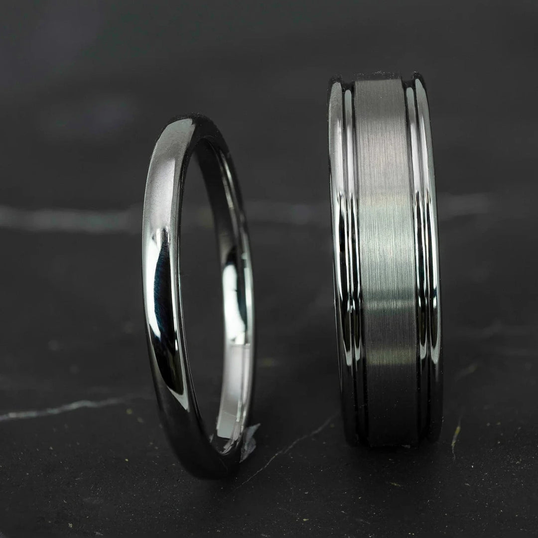 His and hers silver polished 2mm and 6mm tungsten carbide wedding bands on top of black marble stone.