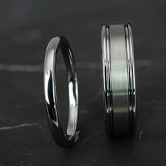 His and hers silver polished 2mm and 6mm tungsten carbide wedding bands on top of black marble stone.