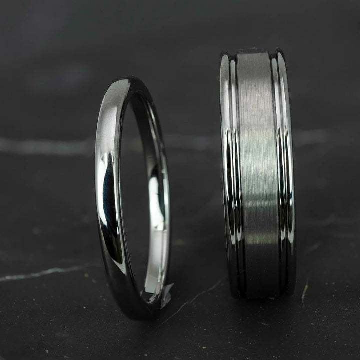 His and hers silver polished 2mm and 6mm tungsten carbide wedding bands on top of black marble stone.