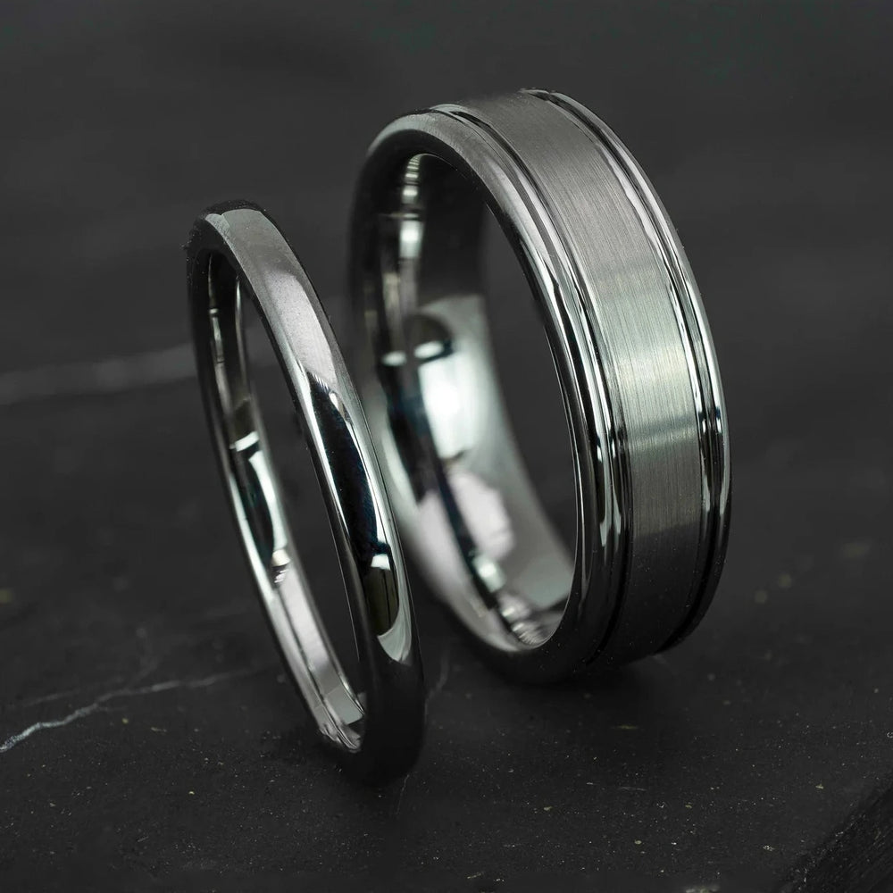 His and hers silver polished 2mm and 6mm tungsten carbide wedding bands on top of black marble stone.