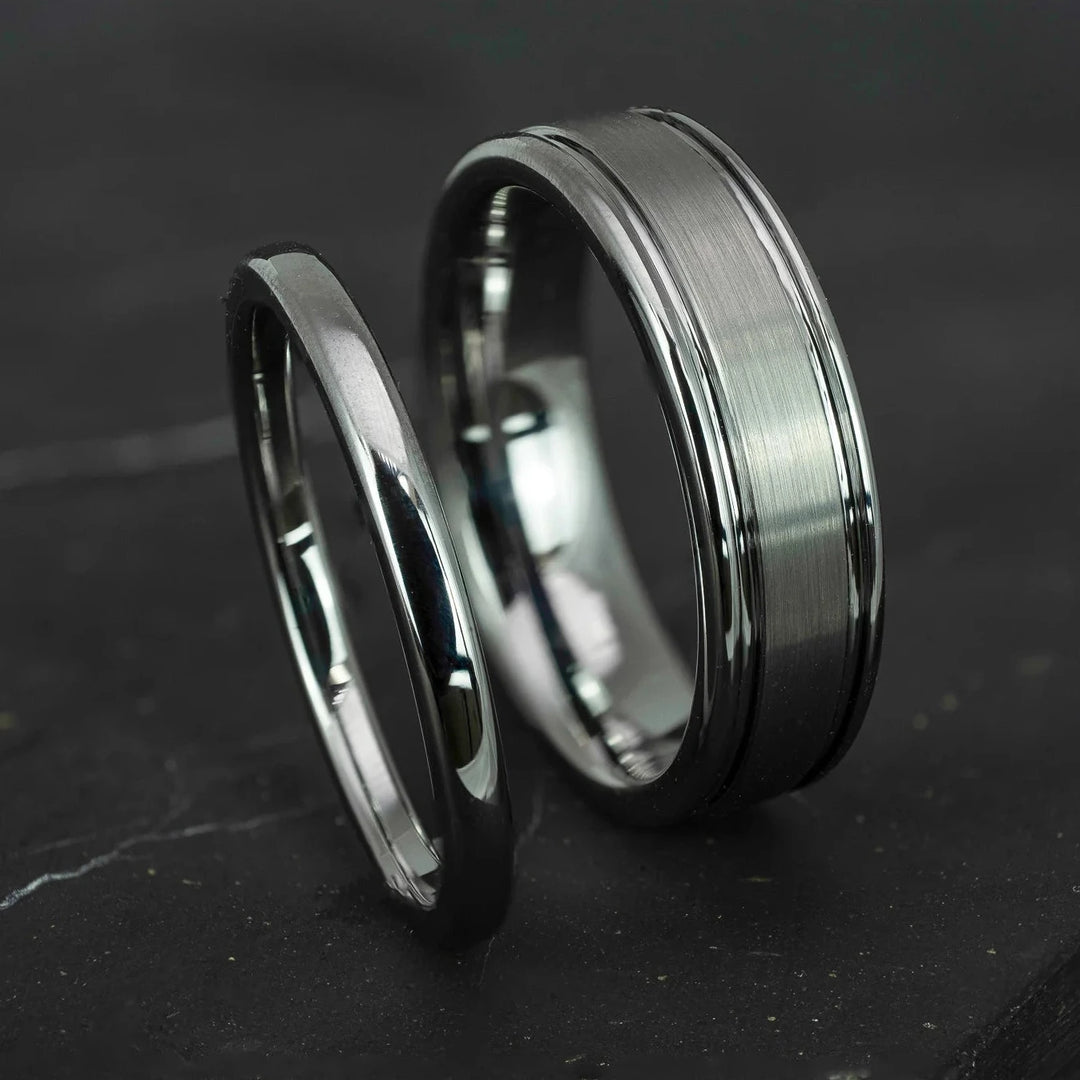 His and hers silver polished 2mm and 6mm tungsten carbide wedding bands on top of black marble stone.