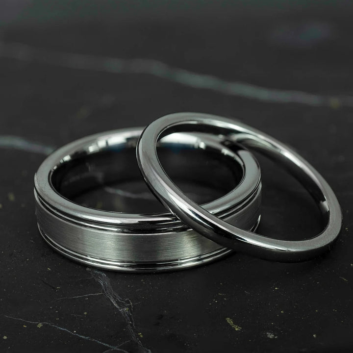 His and hers silver polished 2mm and 6mm tungsten carbide wedding bands on top of black marble stone.